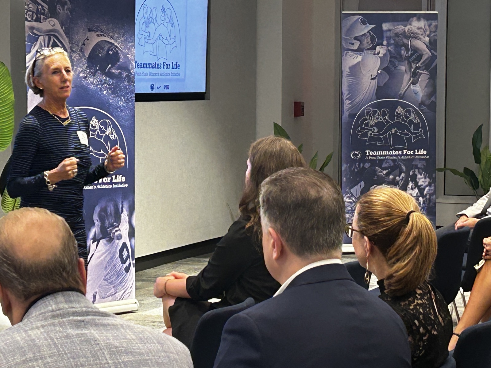 Char Morett Curtiss speaking to guests beside Teammates For Life banners